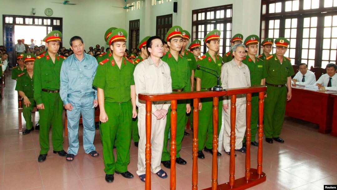 Doan Van Vuon (standing, 4th L), Doan Van Quy (standing, 2nd L) and Doan Van Sinh (standing, 3rd R) stand with policemen in front of the dock at a court during a verdict session in Hai Phong, April 5, 2013.