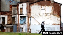 A man walks through a vacant lot where the impression on a demolished home remains on a standing building.