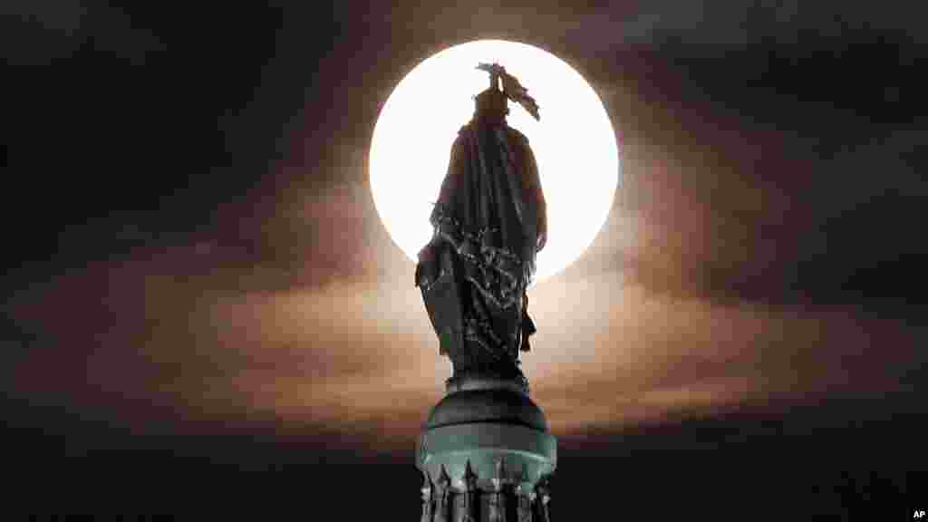 A supermoon rises through the clouds behind the bronze Statue of Freedom atop the U.S. Capitol, Washington, DC, Aug. 10, 2014.