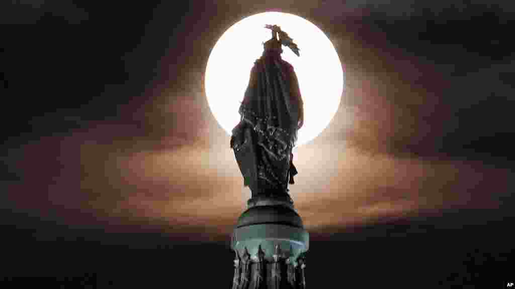 A supermoon rises through the clouds behind the bronze Statue of Freedom atop the U.S. Capitol, Washington, DC, Aug. 10, 2014.