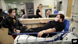 Donnie Cardenas, right, waits in an emergency room hallway alongside roommate Torrey Jewett, left, as he recovers from the flu at the Palomar Medical Center in Escondido, Calif., on Wednesday, Jan. 10, 2018. (AP Photo/Gregory Bull)