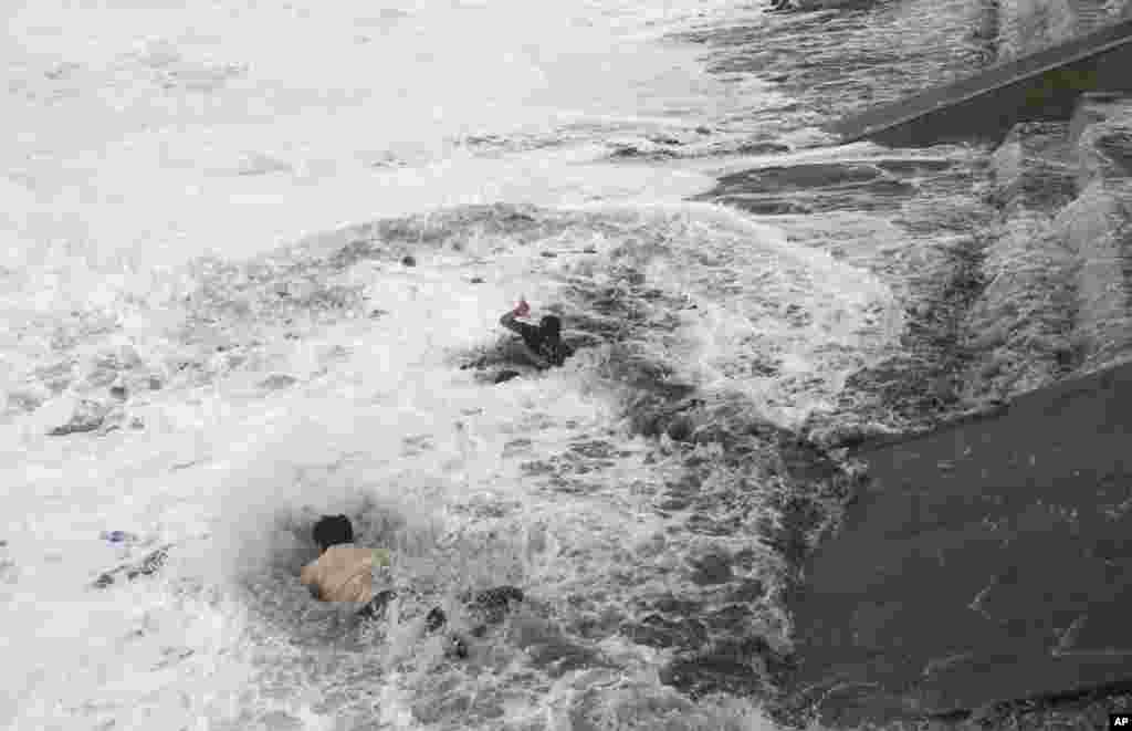 A man, bottom, jumps into the water to rescue a woman, center, who fell due to strong tidal waves on the Bay of Bengal coast at Gopalpur, Orissa, about 285 kilometers (178 miles) north east of Visakhapatnam, India.