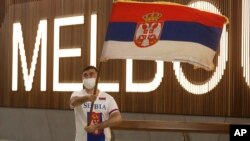 A fan of Serbia's Novak Djokovic waves a Serbian flag in the arrivals area at Melbourne Airport ahead of the Australian Open in Melbourne, Australia, Jan. 6, 2022. Djokovic, who had received a medical COVID-19 vaccine exemption, was barred from entering t