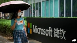 FILE - A woman walks by the Microsoft office building in Beijing, July 20, 2021. The Biden administration and Western allies formally blamed China the day before for a massive hack of Microsoft Exchange email server software.