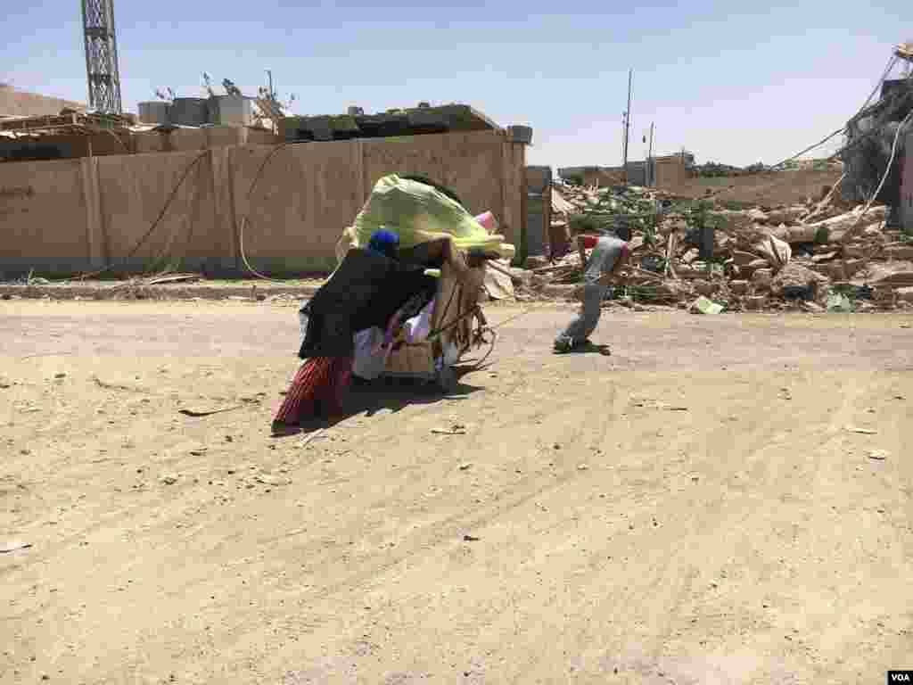 A boy and his mother haul a cart with their family belongings after fleeing their home because of IS-Iraqi forces crossfire in Mosul, Iraq, May 31, 2017. (K.Omar/VOA)