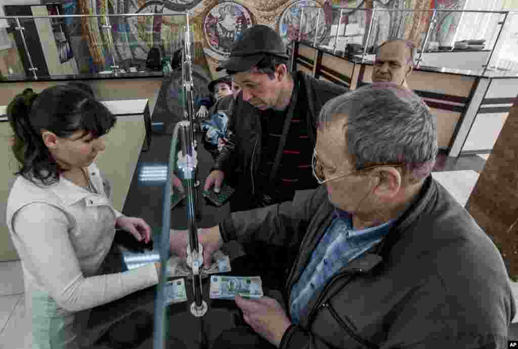 Pensiunan di Krimea mengambil uang pensiun mereka, yang sekarang mulai dibayarkan dalam mata uang rubel Rusia, di kantor pos Simferopol (25/3). (AP/Alexander Polegenko)