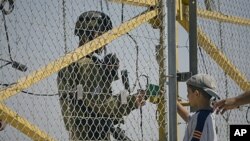 An Israeli soldier checks the identity documents of a Palestinian boy and his father as they wait to cross to their farmland, located behind a section of Israel's separation barrier between the Jewish settlement of Modiin Illit near Ramallah, June 23, 201