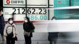 Pedestrians stand in front of an electronic stock board showing Japan's Nikkei 225 index at a securities firm in Tokyo Friday, Feb. 28, 2020. Asian stock markets have fallen further on virus fears after Wall Street endured its drop