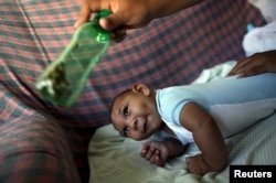 FILE - Jackeline, 26, uses a green bottle to catch the attention of her son, Daniel, who is 4-months old and born with microcephaly, inside of their house in Olinda, near Recife, Brazil, Feb. 11, 2016.