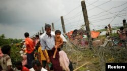 A Rohigya man with child walks along a barbed wire fence in Maungdaw