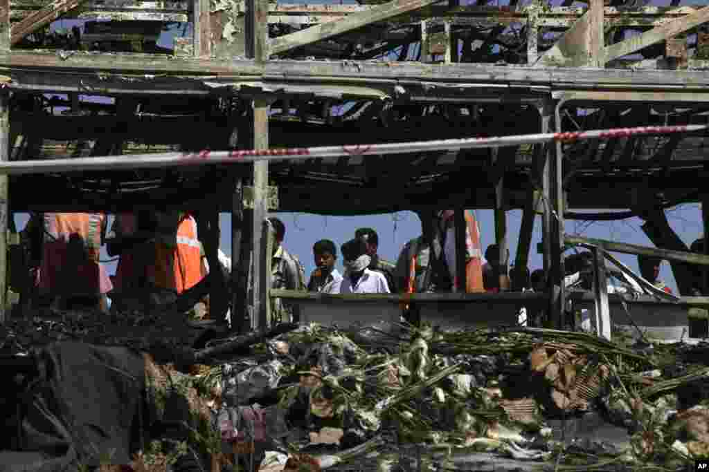 Rescuers and others stand near debris after a bus crashed into a highway barrier and erupted in flames, Mehabubnagar, Andhra Pradesh, India, Oct. 30, 2013.