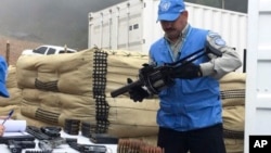 In this photo released by the U.N. mission based in Colombia, a member of U.N. monitoring mission for the Colombian peace process holds a weapon handed over by FARC rebels, as part of last year's peace agreement in Colombia, June 13, 2017.