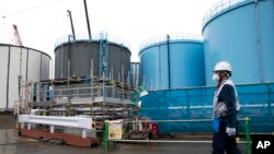 FILE - In this Feb. 23, 2017, photo, an employee walks past storage tanks for contaminated water at the tsunami-crippled Fukushima Dai-ichi nuclear power plant of the Tokyo Electric Power Co. in Japan.