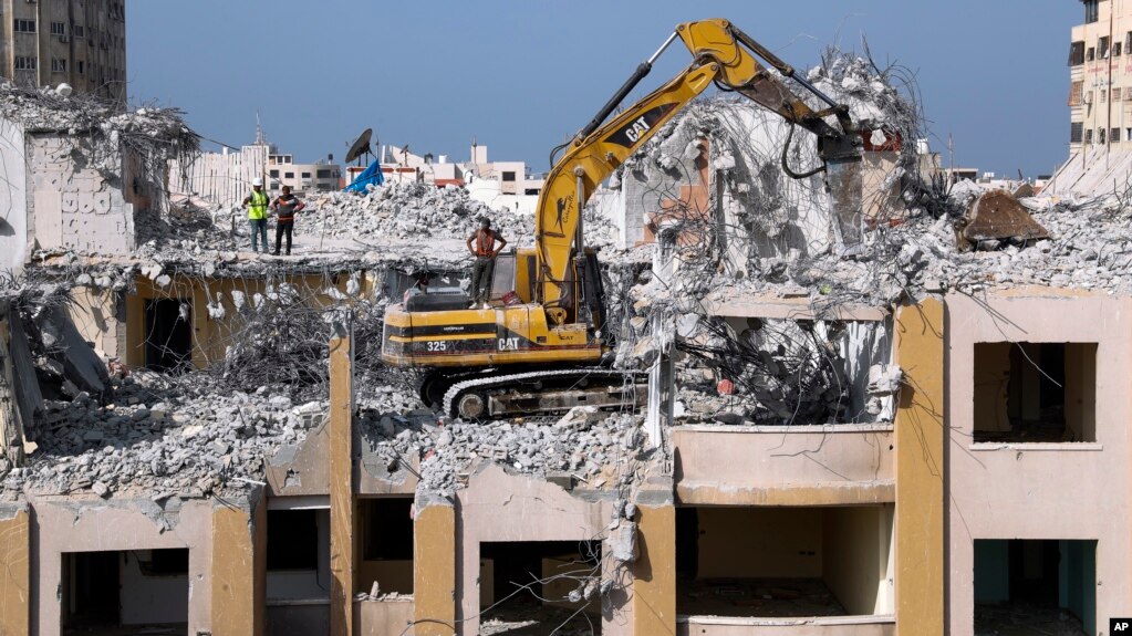 Palestinian workers use a backhoe to break and remove parts of the Al-Jawhara building, that was damaged in Israeli airstrikes during Israel's war with Gaza's Hamas rulers last May, in the central al-Rimal neighborhood of Gaza City, Nov. 16, 2021. (AP Photo/Adel Hana)