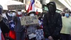 Manifestantes sostienen pancartas que rezan "no más ONU" y "fuera migrantes Ilegales", junto a un manifestante encapuchado a favor de los migrantes durante una protesta contra la inmigración en Santiago de Chile, el 2 de octubre de 2021. 
