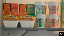 man walks past packages of instant noodles manufactured by Acecook Vietnam