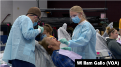 Two volunteer dentists work with a patient at the RAM Clinic, a free mobile health center set up in a school in Charleston, WV. Saturday, Oct. 20, 2018.