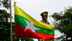 FILE - The Myanmar national flag flies in front of a statue of Gen. Aung San during a ceremony marking the 70th anniversary of his 1947 assassination in Naypyitaw, Myanmar, Wednesday, July 19, 2017. (AP Photo/Aung Shine Oo)