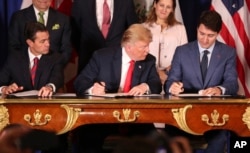 FILE - President Donald Trump looks over at Canada's Prime Minister Justin Trudeau's document as they and Mexico's then-president, Enrique Pena Nieto, sign a new U.S.-Mexico-Canada pact that replaces the NAFTA trade deal, during a ceremony before the start of the G-20 summit in Buenos Aires, Argentina, Nov. 30, 2018.