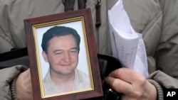 FILE - A portrait of lawyer Sergei Magnitsky, who died in jail, is held by his mother, Nataliya Magnitskaya, as she speaks during an interview with the AP in Moscow, Nov. 30, 2009.