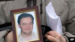 FILE - A portrait of lawyer Sergei Magnitsky who died in jail, is held by his mother Nataliya Magnitskaya, Nov. 30, 2009, as she speaks during an interview with the AP in Moscow, Russia. 