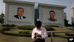 FILE - In this May 5, 2015 file photo, a man sits in front of portraits of the late North Korean leaders Kim Il Sung, left, and Kim Jong Il, right, as he uses his smartphone in Pyongyang, North Korea. (AP Photo/Wong Maye-E, File)