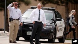 Columbine High School principal Scott Christy, right, joins an officer in watching as students leave the school, April 16, 2019, in Littleton, Colorado. 