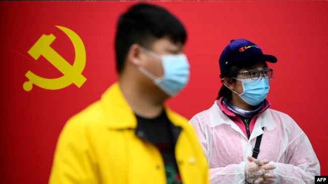 People wearing face masks stand in front of a Communist Party of China flag