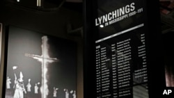 FILE - A monolith listing the names, dates and rationale for the lynching of African-American residents rests in the foreground of a photograph of a burning Ku Klux Klan cross on display in the Mississippi Civil Rights Museum in Jackson, Miss., Nov. 10, 2017. The facility is adjacent to the new Museum of Mississippi History that documents the state's rich history and the diversity of its people. 