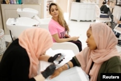 Farah Ibrahim, 25, center, watches as henna is applied on the hands of a customer ahead of the Eid al-Fitr Islamic holiday at the Le'Jemalik Salon and Boutique in Brooklyn, New York, June 21, 2017.
