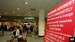 FILE - A woman organizes her carry-on luggage next to a sign explaining new security measures at Miami International Airport.