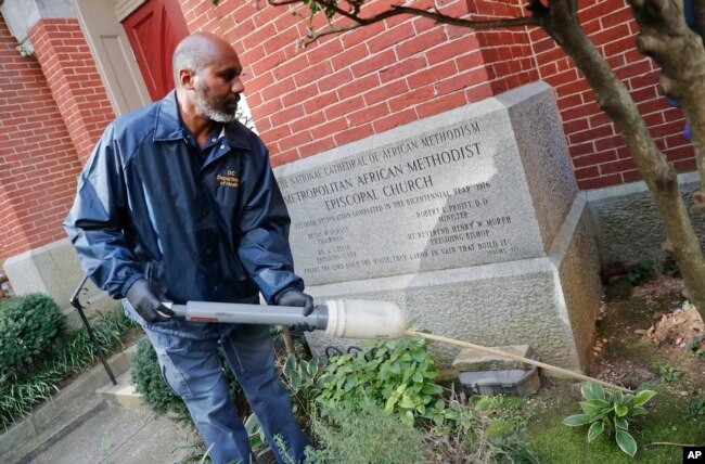 FILE - Pest Control Officer Gregory Cornes, from the D.C. Department of Health's Rodent Control Division, uses a duster to pump poison into rat burrows, found on the grounds of Metropolitan African Methodist Episcopal Church in downtown Washington, Oct. 17, 2019.