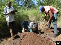 In this April 5, 2019, photo, Stephen Fonseca, center, places a bag with a spine into a small grave as Chief Moses Mukoto, left, writes the time of day in a notebook in Magaru, Mozambique.