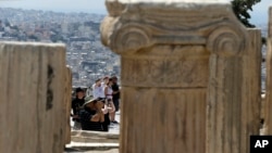 FILE - Tourists take photographs atop of the ancient Acropolis hill in Athens. Bavarian Finance Minister Markus Soeder has called for a tougher stance in negotiations with Greece.