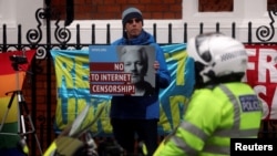 A supporter of WikiLeaks founder Julian Assange holds a placard in front of a police officer, as he stands outside Ecuador's embassy in London, April 6, 2019. 