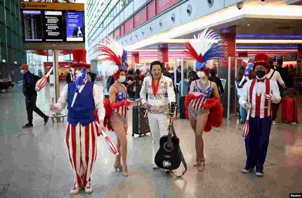 Performers entertain as travelers wait in line to check into Virgin Atlantic and Delta Air Lines flights at Heathrow Airport Terminal 3, in London, following the lifting of restrictions on the entry of non-U.S. citizens to the United States. The restrictions were put in place to slow the spread of the COVID-19.