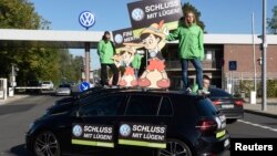 Greenpeace activists hold banners reading "No more lies" as they stand on top of Volkswagen cars in front of VW's "Sandkamp" gate in Wolfsburg, Germany, Sept. 25, 2015. 