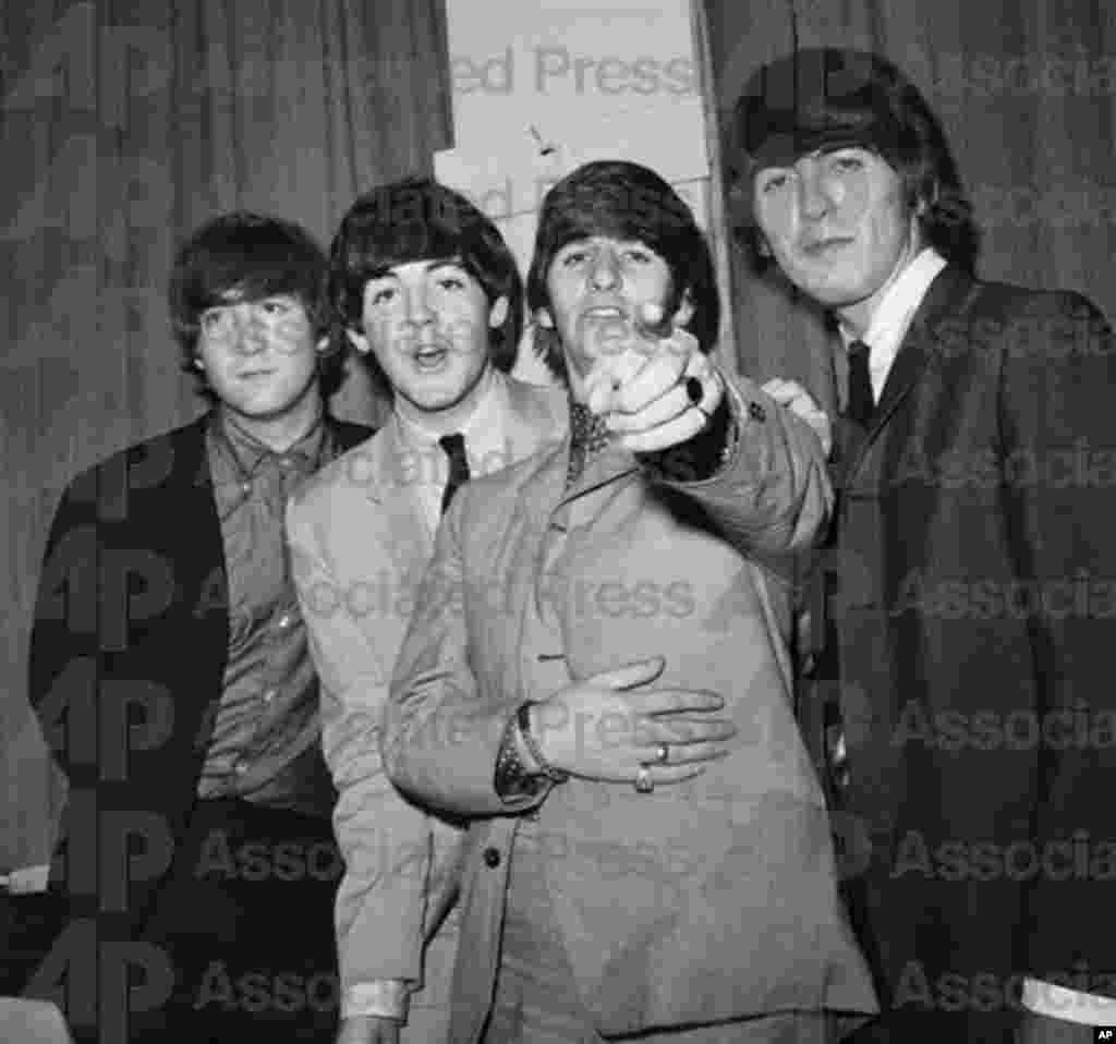 Ringo Starr points at the camera as fellow Beatles John Lennon, Paul McCartney, and George Harrison stand beside him backstage at a charity performance at the Paramount Theater in New York