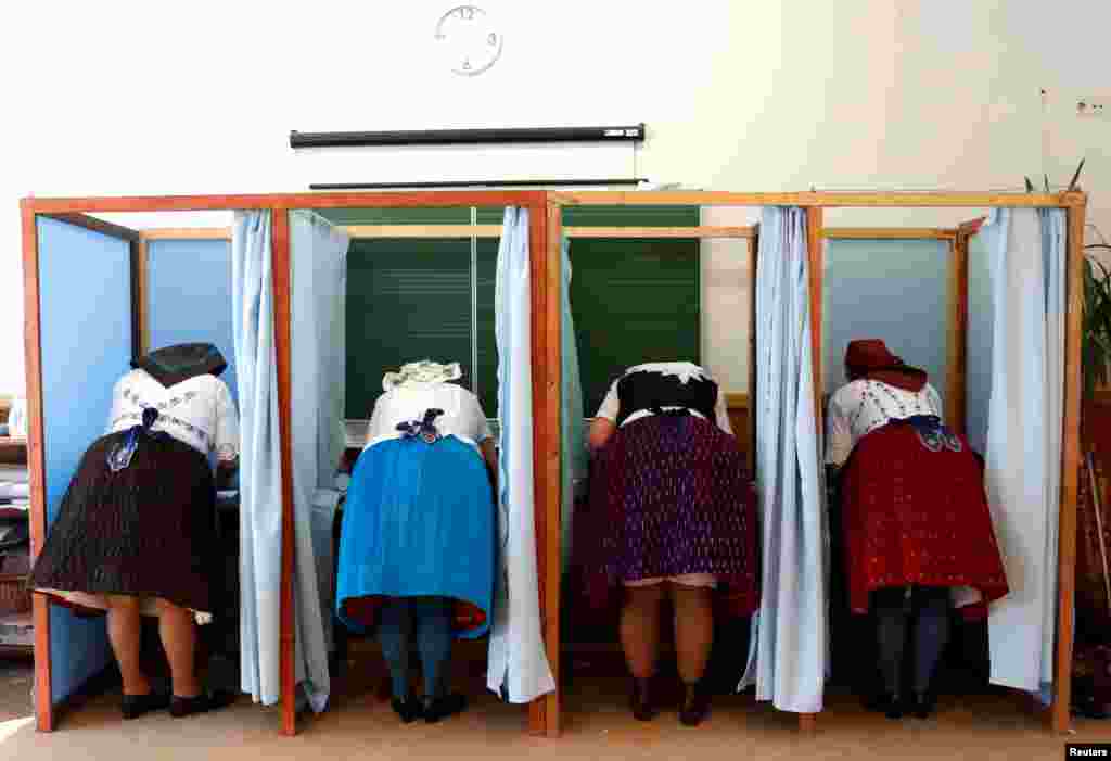 Women, wearing traditional costumes, fill their ballot papers at a polling station during Hungarian parliamentary elections in Veresegyhaz.