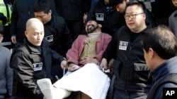 Kim Ki-jong, the suspect of slashing U.S. Ambassador Mark Lippert, in a wheelchair is carried by police officers as he leaves a police station for Seoul Central District Court in Seoul, South Korea, Friday, March 6, 2015.