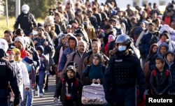 FILE - Slovenian police officers guide migrants towards the Austrian border town of Spielfeld, in the village of Sentilj, Slovenia, Nov. 18, 2015.