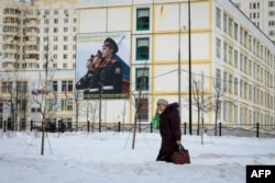 FILE - A woman carrying bags of groceries walks past a school building with a military-themed poster in front of it, on the outskirts of Moscow, Russia, Feb. 27, 2019.