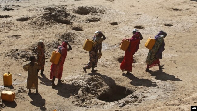 FILE - Women carry jerry cans of water from shallow wells dug in the sand along the Shabelle River bed, which is dry due to drought in Somalia's Shabelle region, March 19, 2016.