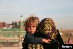 FILE - A woman carries a child as they return with others to the town of Hisha, after the Syrian Democratic Forces (SDF) took control of the area from Islamic State militants, in the northern Raqqa countryside, Syria, Nov. 14, 2016.