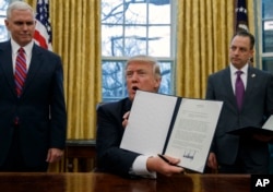 FILE - In this Jan. 23, 2017, photo, Vice President Mike Pence, left, and White House Chief of Staff Reince Priebus, right, watch as President Donald Trump shows off an executive order to withdraw the U.S. from the 12-nation Trans-Pacific Partnership trade agreement.