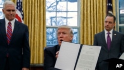 FILE - In this Jan. 23, 2017, photo, then-Vice President Mike Pence, left, and then-White House Chief of Staff Reince Priebus, right, watch as then-President Donald Trump shows off an executive order to withdraw the U.S. from the 12-nation Trans-Pacific Partnership trade pact.