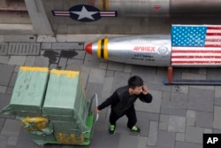 A delivery man calls for directions while pulling a cart of goods past a U.S. apparel store in Beijing Friday, March 23, 2018.