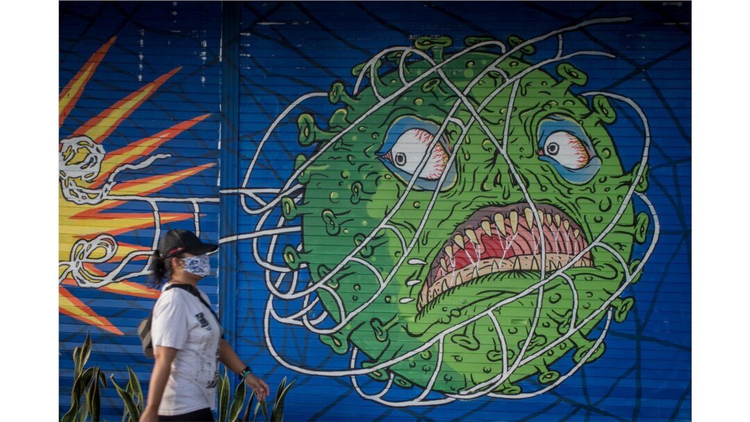 Seorang perempuan mengenakan masker pelindung berjalan melewati mural bertema virus corona saat wabah COVID-19 terus berlanjut di Solo, Jawa Tengah, 21 Februari 2021. (Foto: Antara/Mohammad Ayudha via REUTERS)
