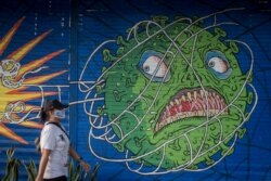 Seorang perempuan mengenakan masker pelindung berjalan melewati mural bertema virus corona saat wabah COVID-19 terus berlanjut di Solo, Jawa Tengah, 21 Februari 2021. (Foto: Antara/Mohammad Ayudha via REUTERS)