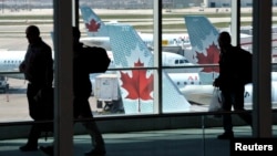 FILE - Passengers walk past Air Canada planes on the runway at Pearson International Airport in Toronto.